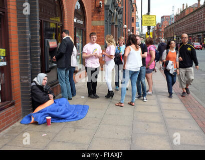 Sans-abri assis au côté d'un point de trésorerie dans les rues de Manchester alors que les gens faire la queue au guichet automatique. photo DON TONGE Banque D'Images