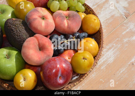 Panier de fruits rouges et jaunes contenant des prunes, pommes Granny Smith, l'avocat, noir & vert raisin, & Paraguayas ou télévision peaches Banque D'Images