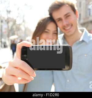 Heureux couple ou des amis de prendre une photo avec un selfies smart phone et montrant un écran vierge à l'appareil photo Banque D'Images