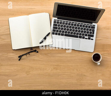 Ordinateur portable, ouvrez le bloc-notes, stylo, lunettes et tasse de café sur la table, des meubles en bois. Vue supérieure avec de l'espace pour votre texte. Banque D'Images