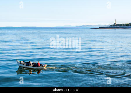 2 hommes dans un petit bateau aller en mer par un beau matin ensoleillé calme clair à Aberystwyth, Ceredigion Mid Wales UK Banque D'Images