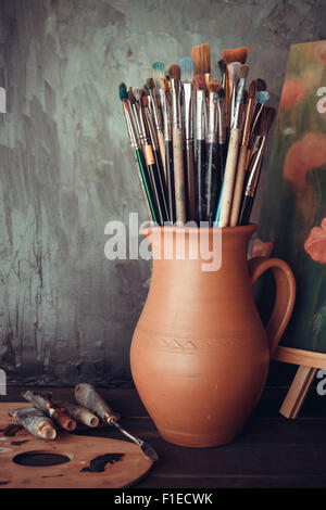 Les pinceaux dans une cruche d'argile potiers, tubes de peinture, palette et la peinture dans un atelier d'artiste. Banque D'Images