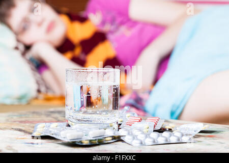 Verre d'eau et des pilules close up et sick girl avec écharpe autour de son cou sur canapé dans la salle de séjour on background Banque D'Images