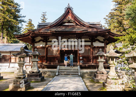 Iwakuni, Japon. Kikko temple shintoïste. Avenue entre deux rangées de lanternes en pierre, toro, menant à salle principale avec jeune couple debout devant la prière. Banque D'Images