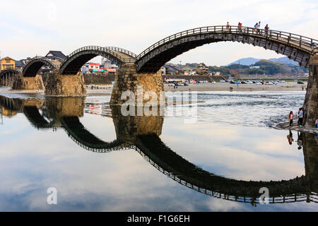 Iwakuni, Japon. La célèbre en bois cintrées multi-pont Kintaikyo et c'est la réflexion dans la rivière Nishiki. Les personnes qui traversent le pont. Banque D'Images