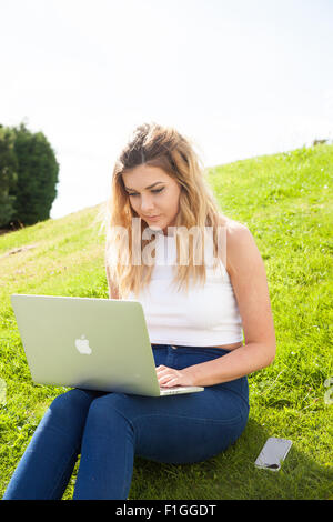 Pretty woman sitting on grass en utilisant un ordinateur portable à l'extérieur. Banque D'Images