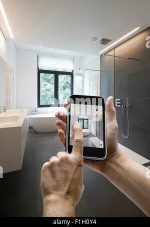 Appareil mobile avec l'homme en tenant les mains photo dans une salle de bains carrelée avec windows vers jardin, les mains sur le côté droit Banque D'Images