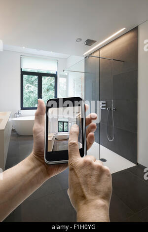 Appareil mobile avec l'homme en tenant les mains photo dans une salle de bains carrelée avec windows vers jardin, les mains sur le côté gauche Banque D'Images