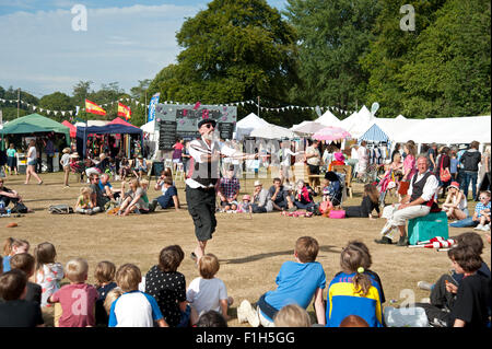 Famille regarder un acte de jonglerie dans le soleil d'été par des stands de nourriture et de tentes au Port Eliot Cornwall Festival Banque D'Images