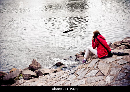 Girl in red jacket assis près de la rivière et à parler dans le cellulaire Banque D'Images