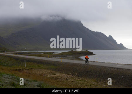 Cycliste solitaire dans un paysage vide, sur l'autoroute de la route 1 en Islande, avec des montagnes en toile de fond, portant une veste haute visibilité Banque D'Images