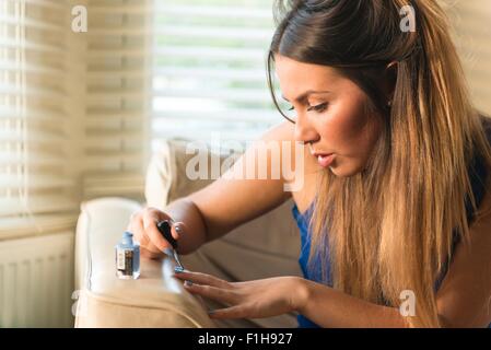 Jeune femme assise sur un canapé, peinture ongles Banque D'Images