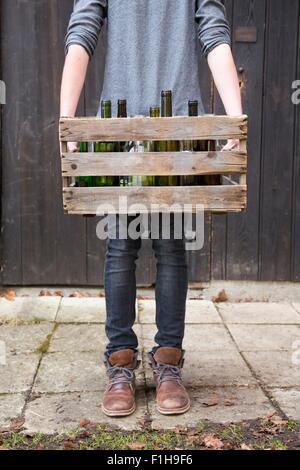 Teenage boy transportant des bouteilles vides dans des caisses en bois Banque D'Images