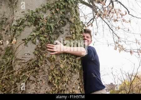 Teenage boy hugging large tronc de l'arbre dans le jardin Banque D'Images