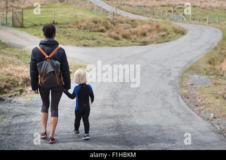 La mère et le fils marche sur route de campagne se tenir la main, vue arrière Banque D'Images