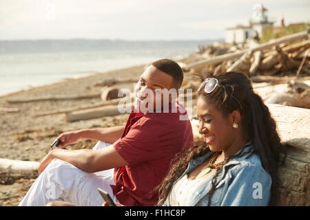 Young couple sitting on beach smiling Banque D'Images