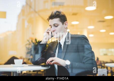 Portrait of young businessman sitting in cafe en utilisant tablette numérique et le téléphone mobile. Banque D'Images