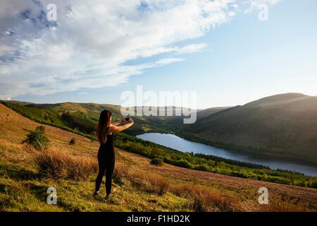 Young woman taking photograph of smartphone réservoir dans Collwn Talybont Glyn valley, Brecon Beacons, Powys, Wales Banque D'Images