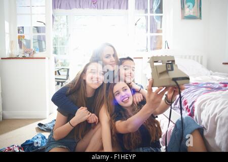 Quatre adolescentes en tenant l'appareil photo instantané dans la chambre selfies Banque D'Images