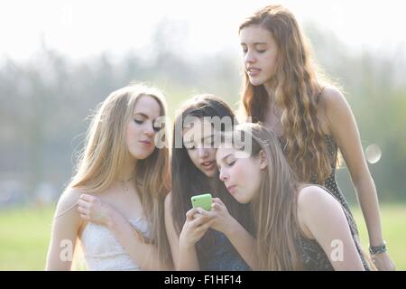 Quatre adolescentes smartphone lecture textes dans park Banque D'Images