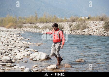 Young male hiker traversant la rivière Toce, Noci, Verbania, Piemonte, Italie Banque D'Images