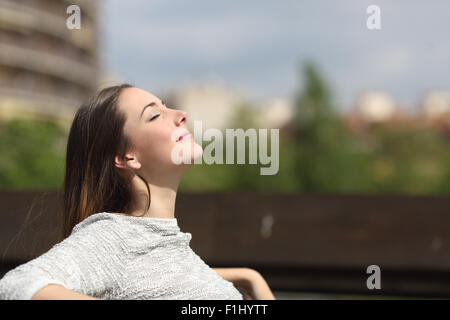Femme urbaine assis sur un banc d'un parc et de respirer profondément l'air frais Banque D'Images