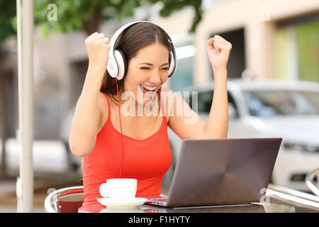 Fille regardant euphorique gagnant un ordinateur portable dans un café portant une chemise rouge Banque D'Images