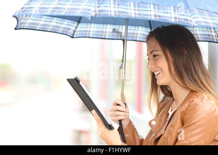 Profil d'une femme lisant ebook ou comprimé sous un parapluie un jour de pluie dans un lieu générique Banque D'Images