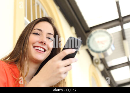 Femme l'achat billet avec un téléphone portable dans un train ou station de bus avec une horloge dans l'arrière-plan Banque D'Images