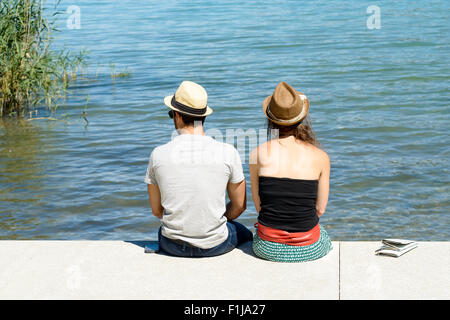Un jeune couple assis sur le bord de l'eau, vue arrière Banque D'Images