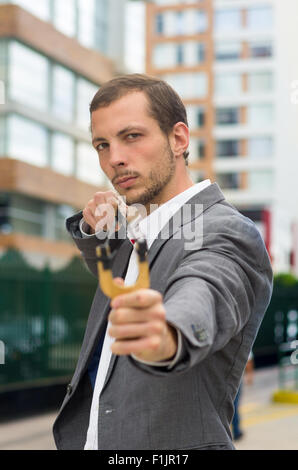 Bel homme d'affaires visant un concentré au fond de la ville urbaine de slingshot Banque D'Images