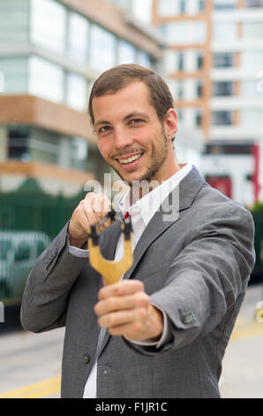 Bel homme d'affaires visant un concentré au fond de la ville urbaine de slingshot Banque D'Images