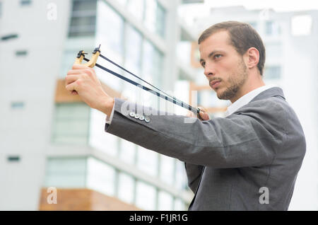 Bel homme d'affaires visant un concentré au fond de la ville urbaine de slingshot Banque D'Images