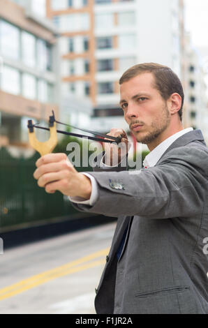 Bel homme d'affaires visant un concentré au fond de la ville urbaine de slingshot Banque D'Images