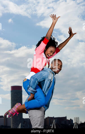 Jeune femme noire assise sur les épaules de l'homme en face de cityscape Banque D'Images