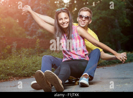 Jeune couple heureux en amour assis sur une planche à roulettes à l'extérieur Banque D'Images