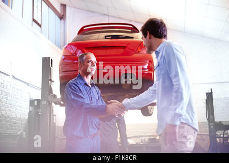 Mécanicien et client handshaking in auto repair shop Banque D'Images