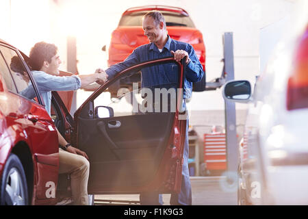 Client et mécanicien de voitures de handshaking in auto repair shop Banque D'Images