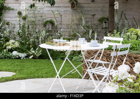 Patio circulaire avec table et chaises, jardin planté de fleurs blanches dans une bordure, clôture blanche peinte et des boîtes à oiseaux Flower Show Royaume-Uni Banque D'Images