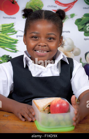 Jeune écolière africaine assis avec son dîner smiling at camera Banque D'Images