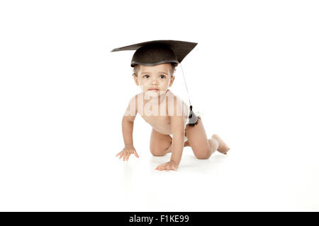 Un bébé ramper devant un fond blanc, portant une graduation cap. Banque D'Images