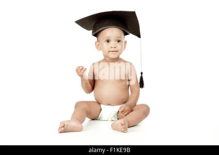 Un bébé assis devant un fond blanc, portant une graduation cap. Banque D'Images