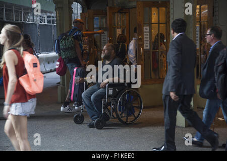 L'homme en fauteuil roulant à la charité de se rendre à la maison du travail et les touristes à l'entrée de Grand Central Terminal de New York. Banque D'Images