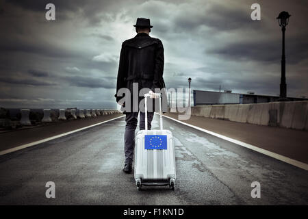 Libre d'un jeune homme vu de dos portant sa valise roulant avec un drapeau européen, avec un effet dramatique Banque D'Images