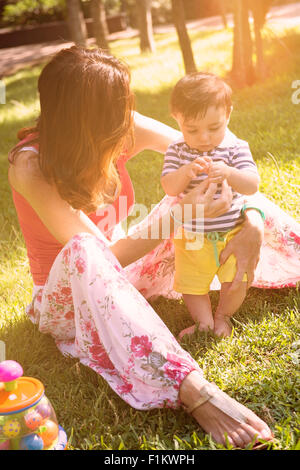 Mère et fils de 7 mois jouant joyeusement sur l'herbe filtre appliqué à chaud Banque D'Images