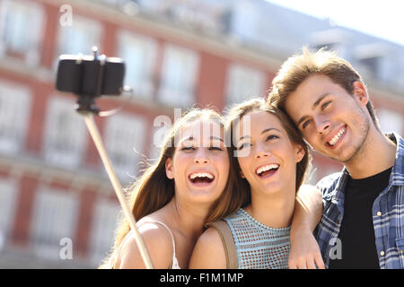 Groupe de trois amis touristiques en tenant avec smart phone selfies monopode main dans la rue Banque D'Images