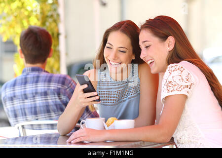 Deux amis heureux ou soeurs partageant un téléphone intelligent dans un café à la terrasse à l'appareil en été Banque D'Images