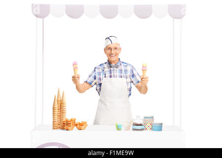 Portrait d'un vendeur de glaces mature tenant deux cornets et debout derrière un kiosque isolé sur fond blanc Banque D'Images