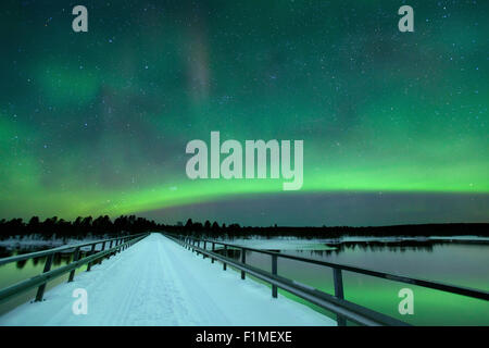 Des aurores boréales) sur un pont et une rivière dans un paysage d'hiver enneigé en Laponie finlandaise. Banque D'Images