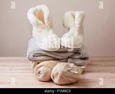 Paire de Chaussons en peau de mouton d'hiver chaud (alpaga), fil de laine , aiguille à tricoter , tas de vêtements en laine chaude (Selective focus) Banque D'Images